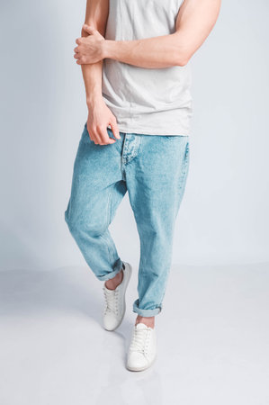 Young muscular man in a light T-shirt and black jeans on a white background. Copy, empty space for text.の写真素材