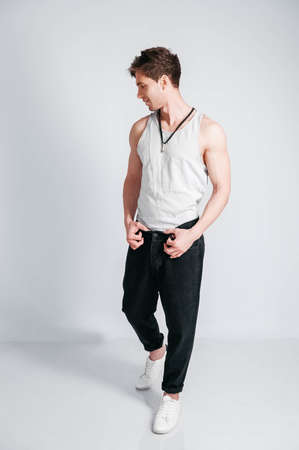 Young muscular man in a light T-shirt and black jeans on a white background. Copy, empty space for text.の写真素材