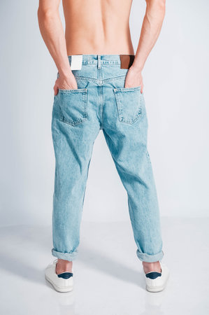 Young muscular man in a light T-shirt and black jeans on a white background. Copy, empty space for text.の写真素材