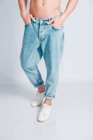 Young muscular man in a light T-shirt and black jeans on a white background. Copy, empty space for text.の写真素材