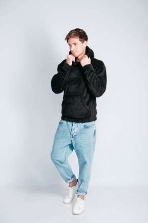 Young muscular man in a light T-shirt and black jeans on a white background. Copy, empty space for text.の写真素材