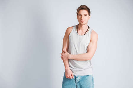 Young muscular man in a light T-shirt and black jeans on a white background. Copy, empty space for text.の写真素材