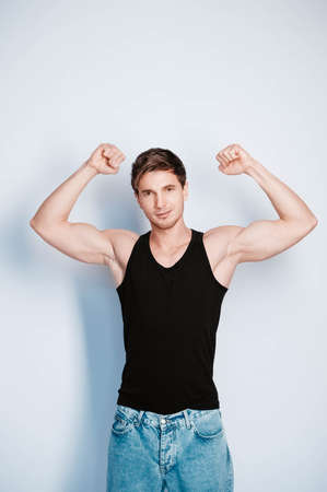 Young muscular man in a light T-shirt and black jeans on a white background. Copy, empty space for text.の写真素材