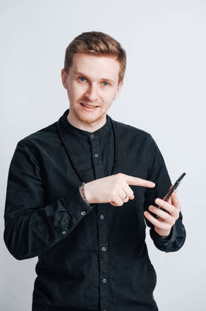 Young man in a black shirt with a smartphone in his hands on a white background. Copy, empty space for text.の写真素材