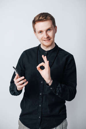 Young man in a black shirt with a smartphone in his hands on a white background. Copy, empty space for text.の写真素材