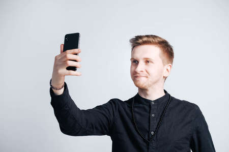 Young man in a black shirt with a smartphone in his hands on a white background. Copy, empty space for text.の写真素材