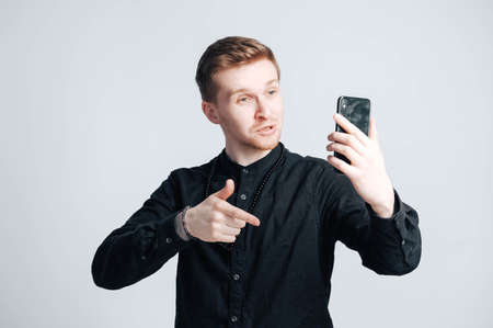 Young man in a black shirt with a smartphone in his hands on a white background. Copy, empty space for text.の写真素材
