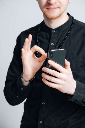 Young man in a black shirt with a smartphone in his hands on a white background. Copy, empty space for text.の写真素材