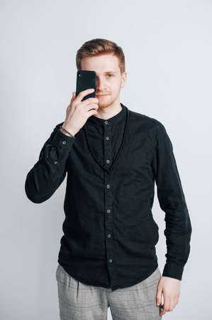 Young man in a black shirt with a smartphone in his hands on a white background. Copy, empty space for text.の写真素材