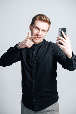 Young man in a black shirt with a smartphone in his hands on a white background. Copy, empty space for text.の写真素材