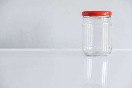 Empty glass jar with red cover on white table background. Copy, empty space for text.の写真素材