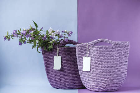 Two purple handmade knitted bag with flowers on a purple and light blue background. Copy, empty space for text.の写真素材