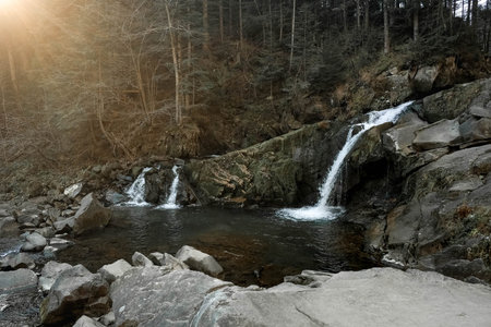 Small cascading waterfall among the rocks and forest. Beautiful mountain landscape. Copy, empty...