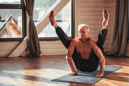 Caucasian senior man practicing yoga classic asana in studio, training in front of a window. Copy, empty space for text.の写真素材