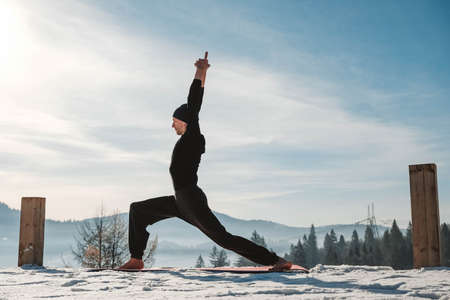 Man sitting in a meditative position in front of amazing sunset on the winter mountains. Copy, empty space for text.の写真素材