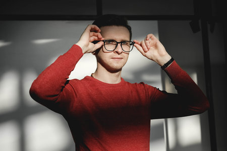Young man in a red sweater on a white background with shadows from the light. Copy, empty space for text.の写真素材