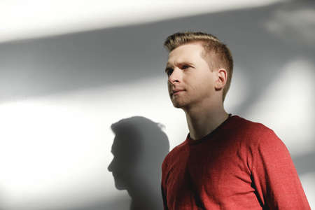 Young man in a red sweater on a white background with shadows from the light. Copy, empty space for text.の写真素材