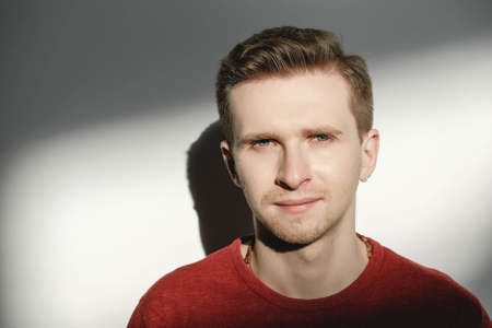 Young man in a red sweater on a white background with shadows from the light. Copy, empty space for text.の写真素材