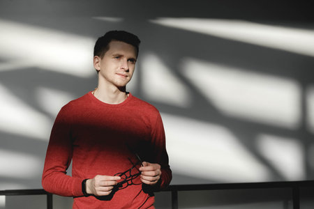Young man in a red sweater on a white background with shadows from the light. Copy, empty space for...