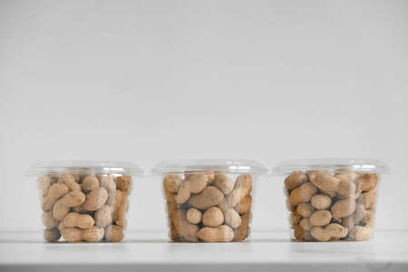 Organic dry peanuts in three transparent plastic bowls on a white table. Copy, empty space for text.の写真素材