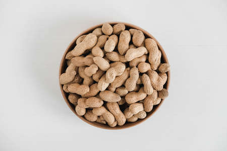 Dry peanuts in a wooden bowl on a white background. Top view. Copy, empty space for text.の写真素材