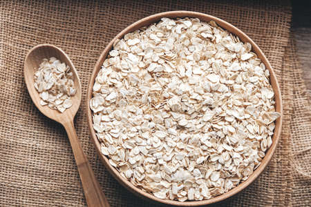 Dry oatmeal in a wooden bowl and spoon on a linen fabric background. Copy, empty space for text.の写真素材