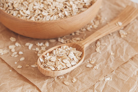 Dry oatmeal in a wooden bowl and spoon on kraft paper on a white background. Top view. Copy, empty space for text.の写真素材