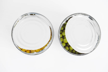 Two open cans with corn and peas on a white background. Top view. Copy, empty space for text.の写真素材