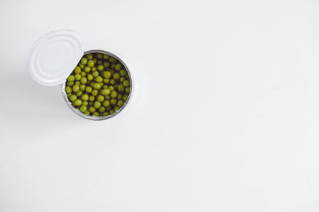 Canned green sweet peas in an open aluminum metal can on a white table. Top view. Copy, empty space for text.の写真素材