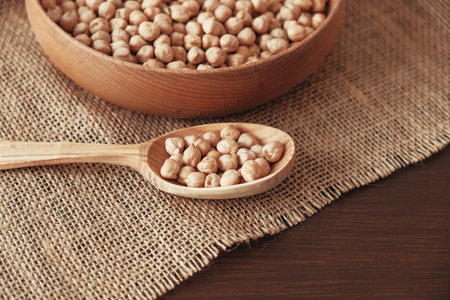 Dry chickpeas in a wooden plate and spoon on a brown wooden background. Copy, empty space for text.の写真素材
