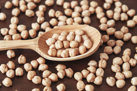 Raw chickpeas in a wooden spoon scattered on a wooden background. Top view. Copy, empty space for text.の写真素材