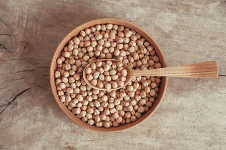 Raw chickpeas in a wooden plate and spoon on an rustic wooden background. Top view. Copy, empty space for text.の写真素材