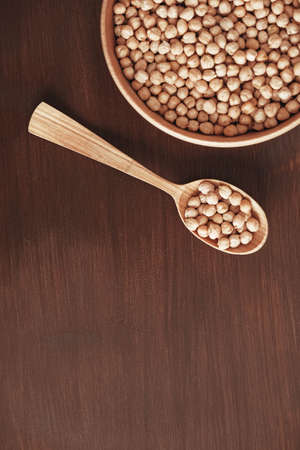 Dry chickpeas in a wooden plate and spoon on a brown wooden background. Top view. Copy, empty space for text.の写真素材