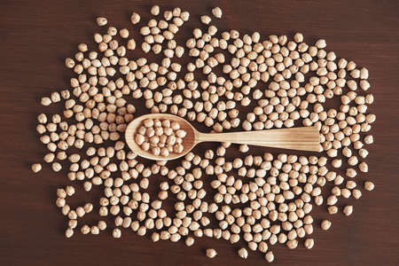 Raw chickpeas in a wooden spoon scattered on a wooden background. Top view. Copy, empty space for text.の写真素材