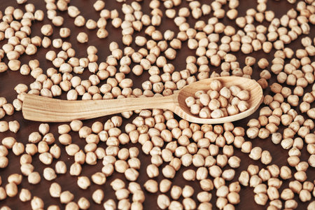 Raw chickpeas in a wooden spoon scattered on a wooden background. Top view. Copy, empty space for...