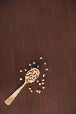 Raw chickpeas in a wooden spoon scattered on a wooden background. Top view. Copy, empty space for text.の写真素材