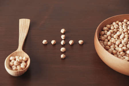 Dry chickpeas in a wooden plate and spoon on a brown wooden background. Top view. Copy, empty space for text.の写真素材
