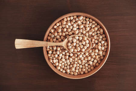 Dry chickpeas in a wooden plate and spoon on a brown wooden background. Top view. Copy, empty space for text.の写真素材