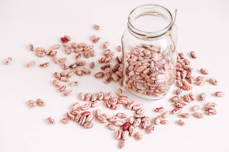 Dry beans in a glass jar scattered on a white table background. Copy, empty space for text.