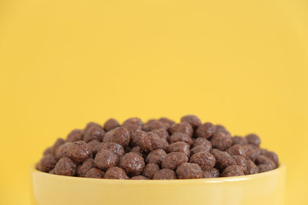 Chocolate cereal corn balls in a yellow bowl on a yellow background. Copy, empty space for text.