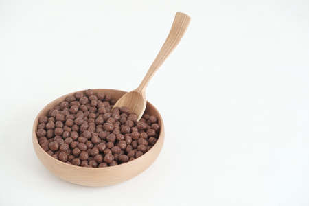 Chocolate corn balls in a wooden bowl and spoon on a white background. Copy, empty space for text.の写真素材
