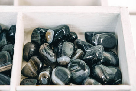 Black polished agate in wooden white boxes. Top view. Copy, empty space for text.