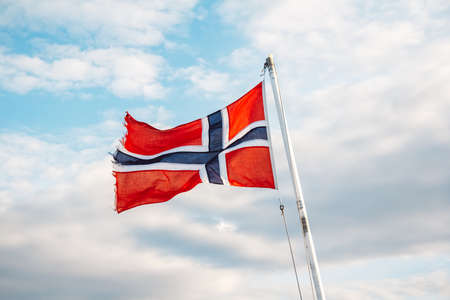 Norway flag on a background of blue sky with clouds. Space for your text message or promotional content.の写真素材