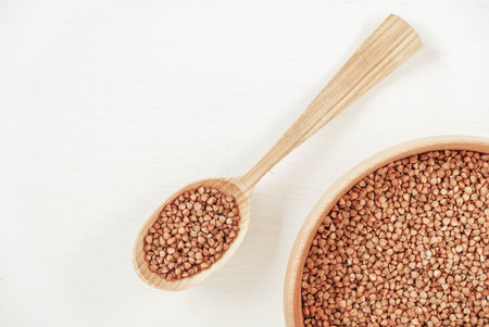 Buckwheat kernels in wooden bowl and spoon on white background. Top view. Copy, empty space for text.の写真素材