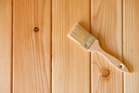 Paint brush with bristles and a wooden handle on natural wooden boards. Top view. Copy, empty space...