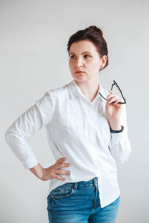 Portrait of a serious beautiful woman in optical glasses and a white shirt on a white background. Copy, empty space for text.の写真素材
