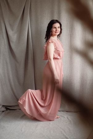Beautiful brunette woman in a pink dress on a background of linen fabric. Copy, empty space for text.の写真素材