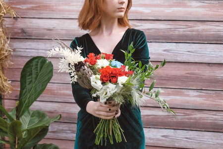 Beautiful girl in a green dress holding a bouquet of flowers and greenery on a wooden background. Copy, empty space for text.の写真素材