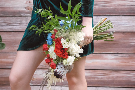 Beautiful girl in a green dress holding a bouquet of flowers and greenery on a wooden background. Copy, empty space for text.の写真素材