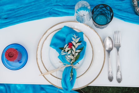 White banquet table covered with blue cloth, served with plates, cutlery, glasses, candles and flower arrangements. Top view. Copy, empty space for text.の写真素材